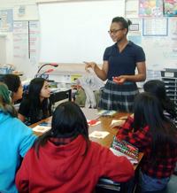 girls in a classroom listening to a young woman standing at front